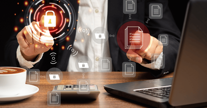 An image of a person sitting at a desk with a latte and computer on the desk with holographic images of a security lock and a paper in front of the person and they are selecting both of these icons.